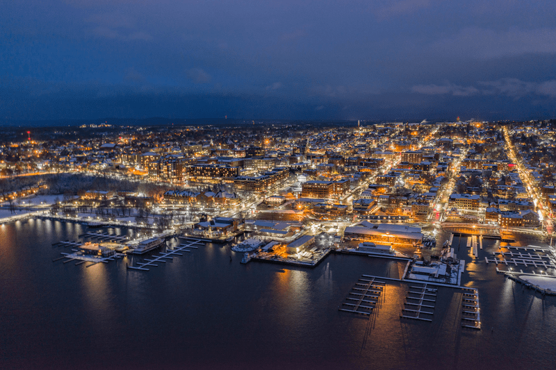 Seen from above, a historic downtown at night, with lights reflecting on a lake.