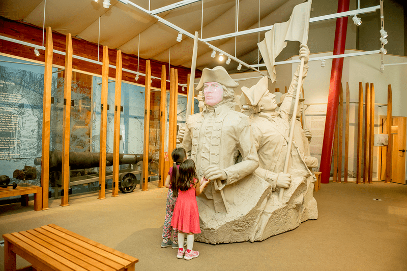 Two kids look at a statue of revolutionary-era figures.