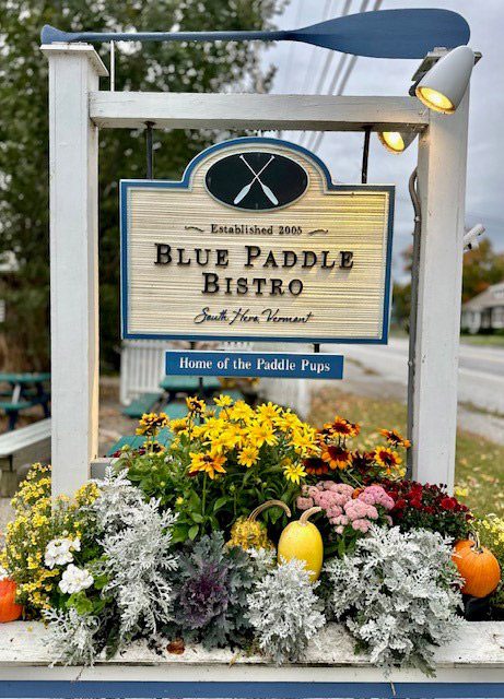 A sign that reads Blue Paddle Bistro is decorated with mums, pumpkins, and other fall-related trimmings.