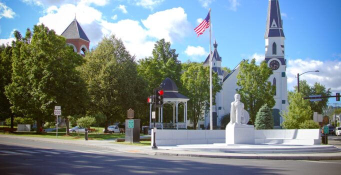 Seen from across a street, a large granite sculpture of a person with a shield.