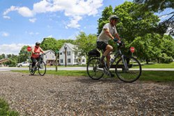 Two people ride bicycles along a gravel path in the summer.