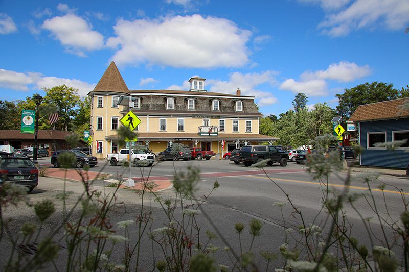 Seen from across a paved road, a yellow building with an open flag and cars parked in front.