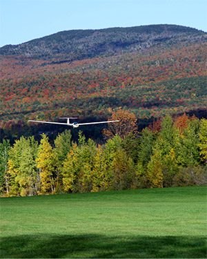 A glider plan lands on a grassy field in the fall.