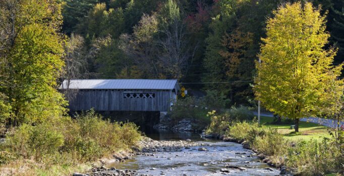 A covered bridge spans a flowing river in the fall.