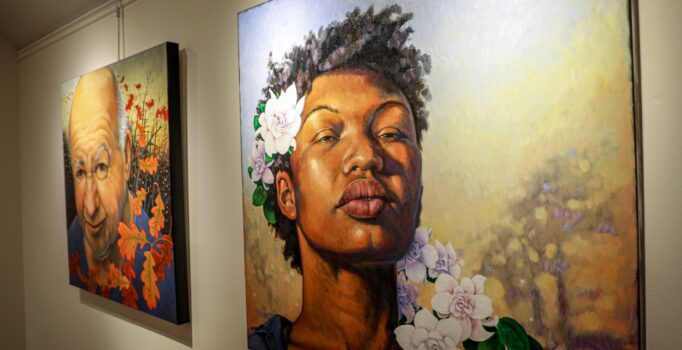 Paintings on a gallery wall of people’s faces with flowers.