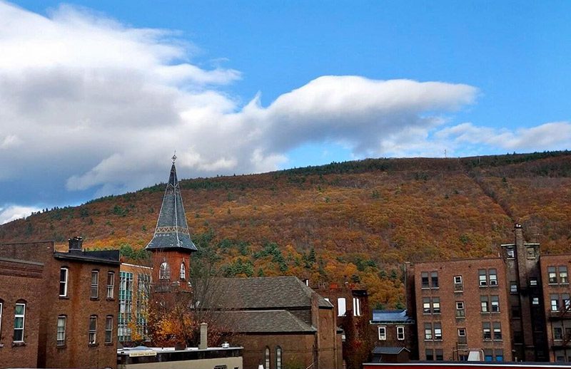 The tops of buildings are seen against a backdrop of trees in the fall.