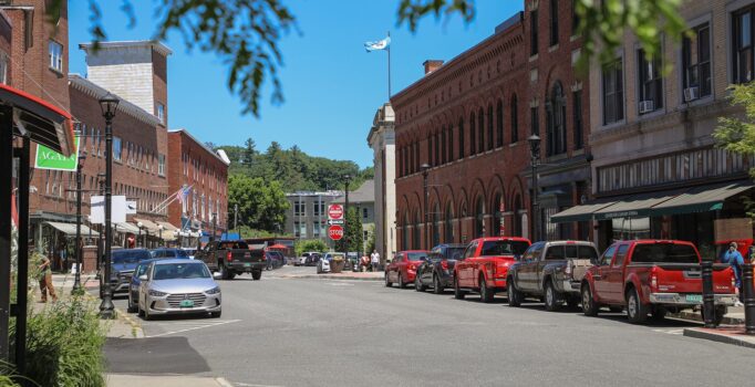 Cars line a paved road through a small rural town.
