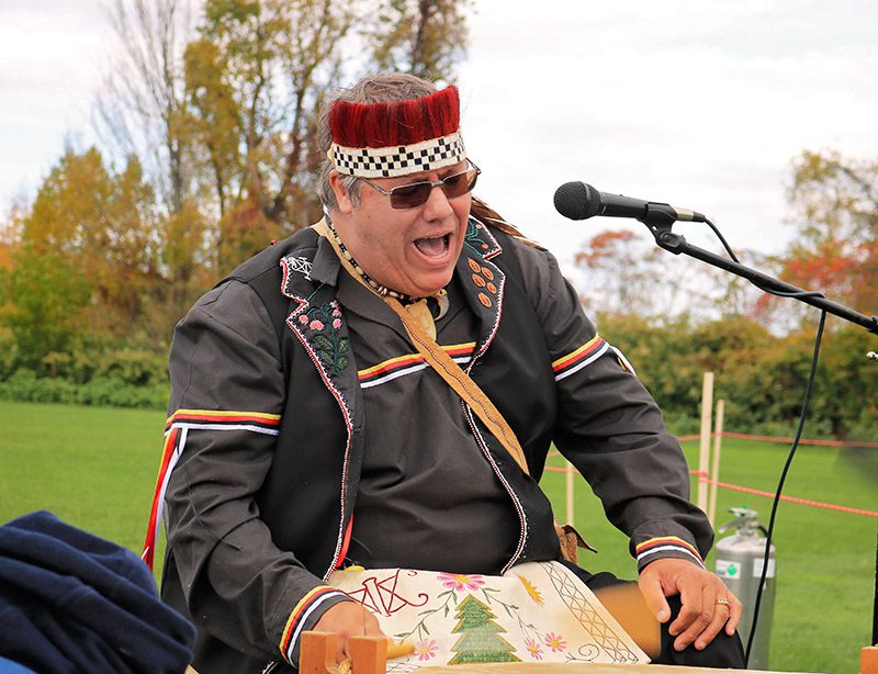 A person speaks into a microphone at an outdoor festival in the fall.