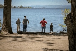 Four people look out across a large body of water from a sandy beach.