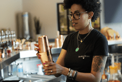 A person mixes a drink with a shaker in a bar.