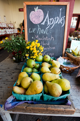 Baskets of pears sitting in front of a sign slightly hidden by yellow flowers