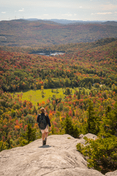 A person walks along an exposed mountain ridge with foliage seen through the valley.