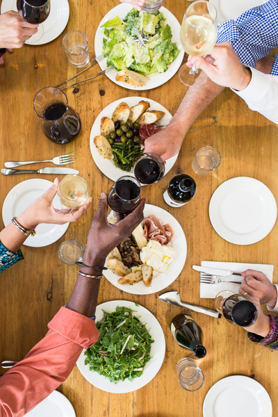 A top down view of people clinking glasses above a table of food.