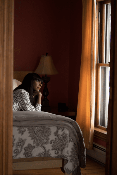 A person laying on a bed looks out a window.