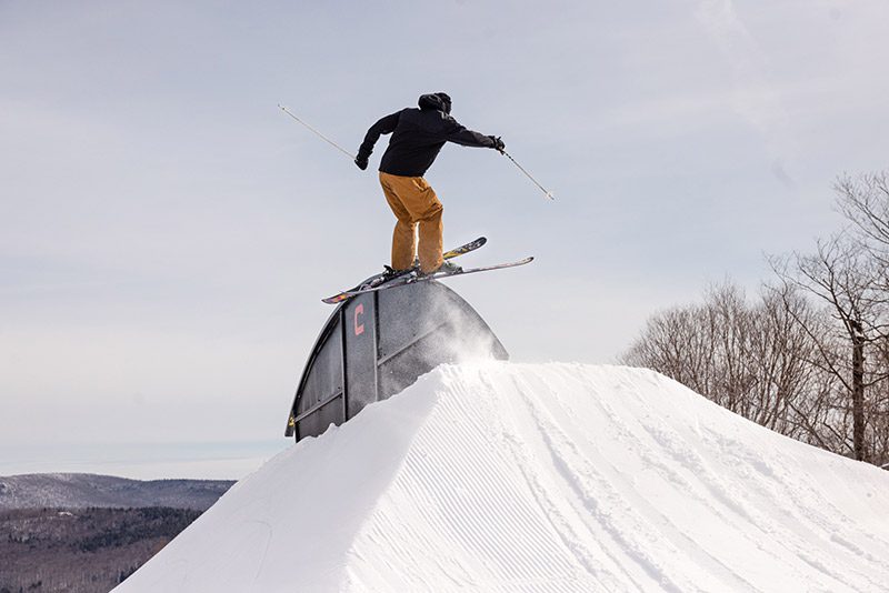 A person on downhill skis, rides a rail in the terrain park.