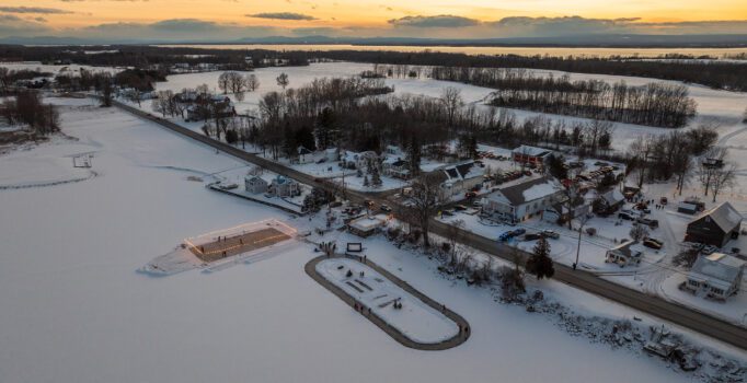 Seen from above, a small town borders a frozen lake with a plowed ice rink and skate oval.