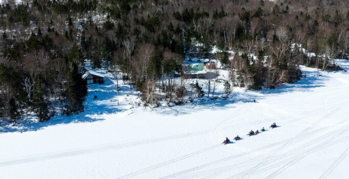 Seen from above, a line of snowmobiles traverse a frozen lake.