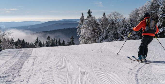 A person wearing an orange jacket skis down a groomed slope.