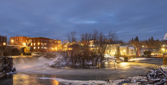 A town with brick buildings is lit up at night in the winter.