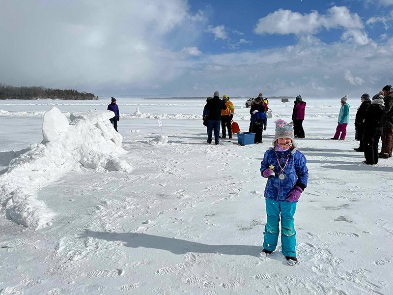 An adolescent holds a medal won during a competition on the ice of a frozen lake.