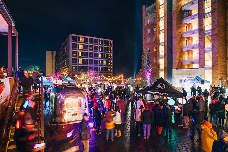 A large group of people attend an event outside on an urban street at night.