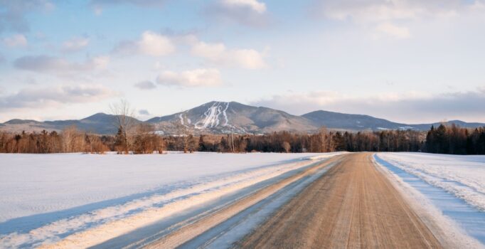 As seen from afar, along a dirt road, a ski resort covered in snow.