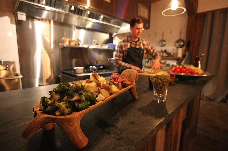 A chef prepares a meal behind a spread of appetizers on a wooden dish.