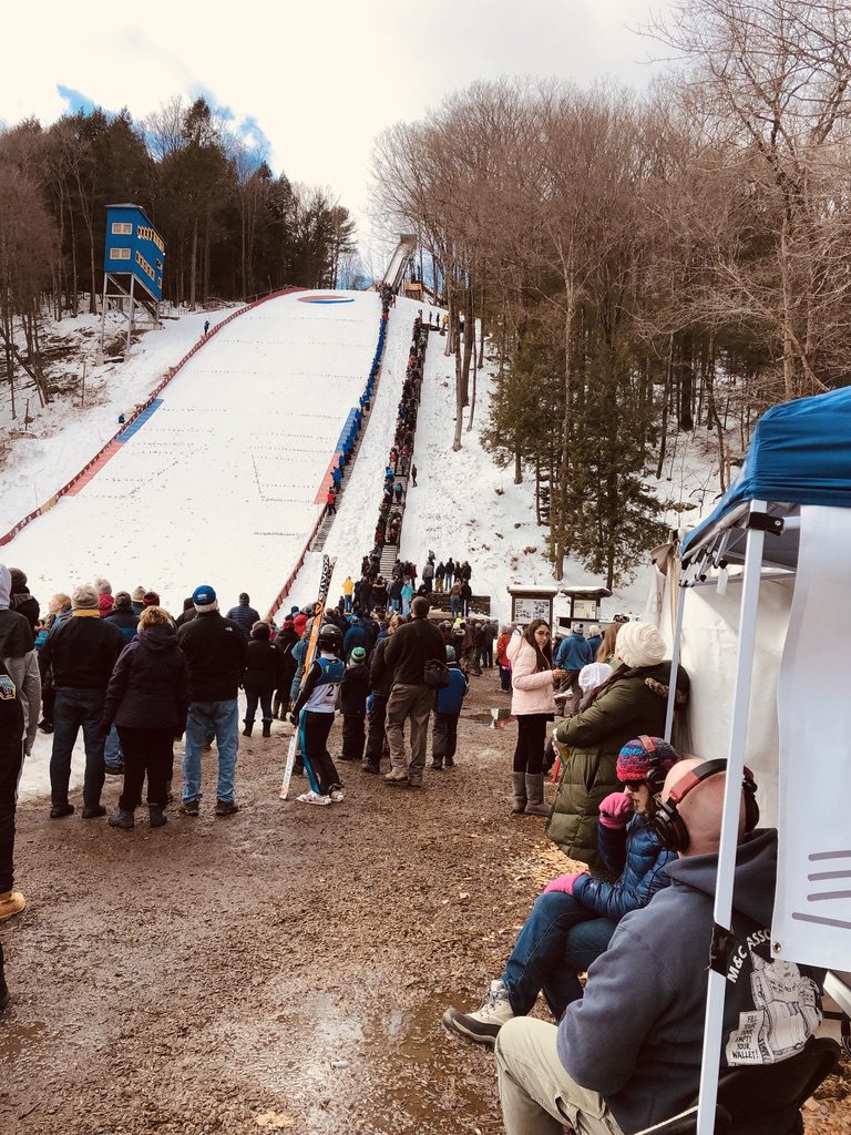 A group of people watch at the bottom of a ski jump to watch a competition.