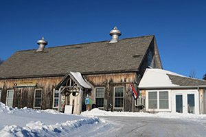 The outside of a wooden building in the snow on a sunny day.