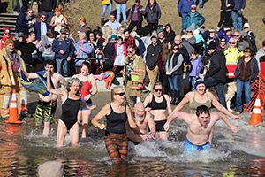 A group of people enter a cold lake in the winter on a sunny day.