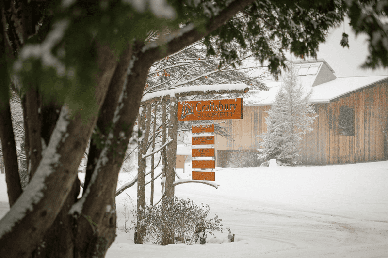 A Craftsbury Outdoor center hangs in front of a wood building on a snowy day.