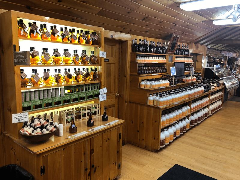 Rows of maple syrup are on display on wooden fixtures in a store.