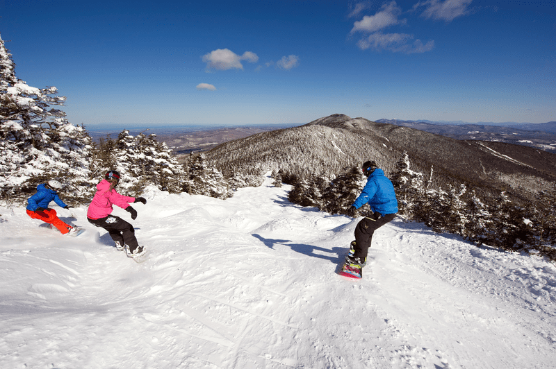 Three people snowboard down a snowy alpine slope.