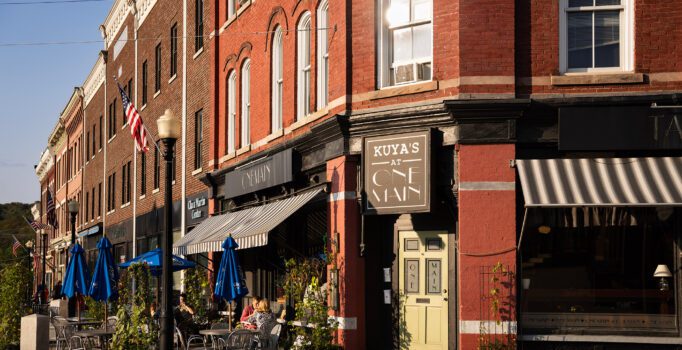 Red brick buildings with outdoor seating are seen in a rural downtown.