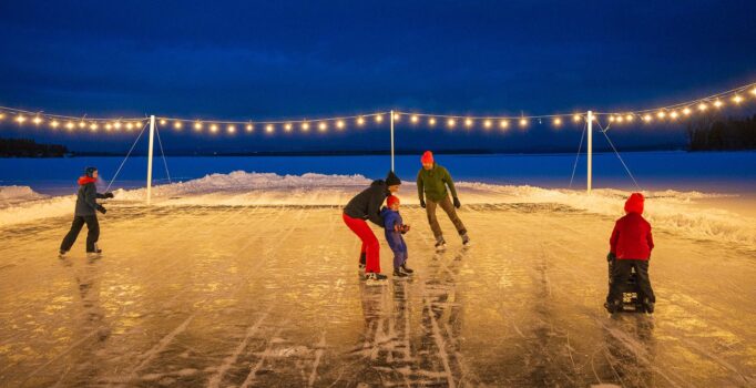 Four people skate on a frozen lake under lights at night.