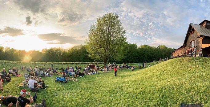 A wide image of people sitting on the grass outside in the summer listening to live music at a vineyard.