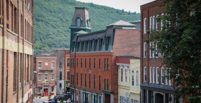 A historic downtown with brick buildings lining a bustling street and mountains visible in the background. 