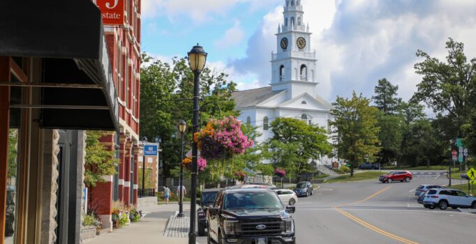 A historic downtown with a white church and brick buildings lining the sidewalks where people are walking.