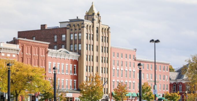 A row of brick buildings overlook a large parking lot with cars.