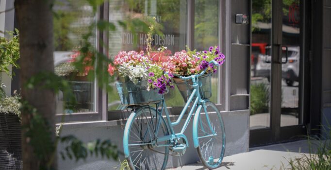 An old bicycle upcycled as flower-pot arrangement in front of a storefront.