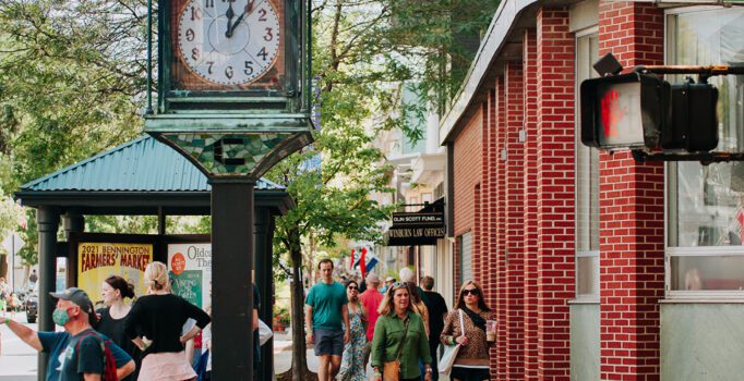 People walk along a main street lined with brick buildings and shops.