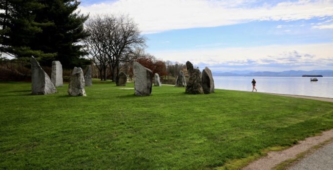 Rocks are arranged in a circles on a mowed lawn overlooking a large lake in the spring.