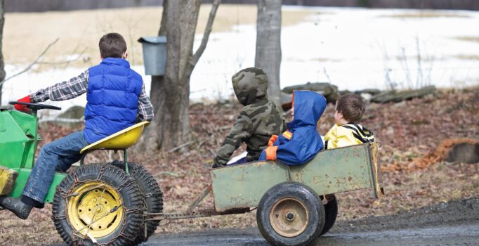 A small tractor pulls a small trailer with children riding.