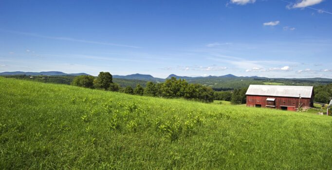 Seen from afar, a red barn in a grassy field on a warm day.