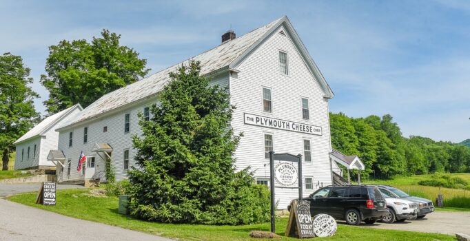 A white building that reads Plymouth Cheese against a blue sky in the summer.