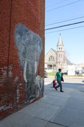 A person walking past a mural of an elephant on a brick wall.