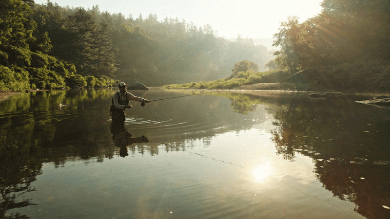 A person casts a fly rod in a calm river.