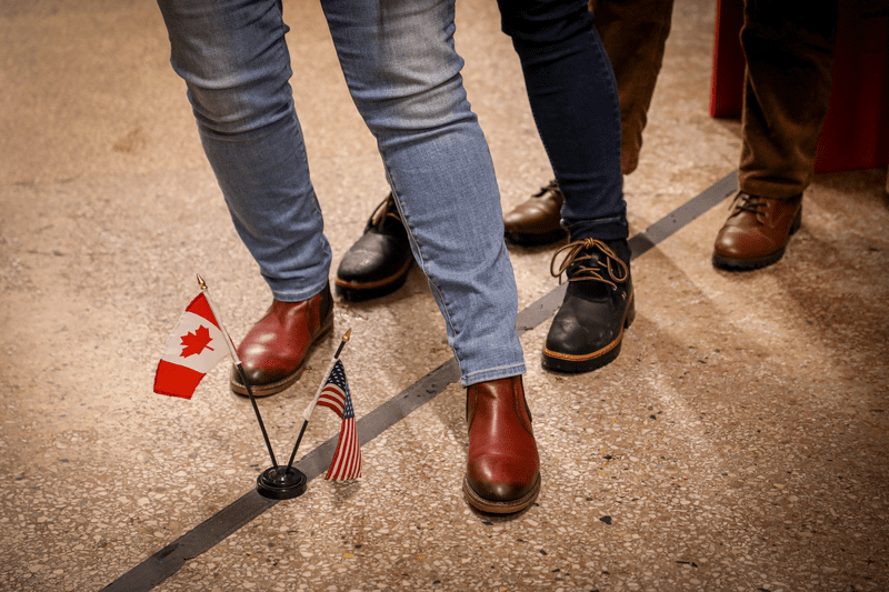 Three people straddle a line on the floor separating Canada from the United States.