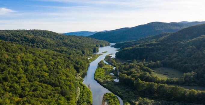 Seen from above, a river winding through tree-covered mountains on a warm day.
