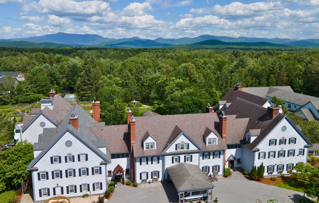 Seen from above, a white lodge on a sunny summer day with mountains visible behind.
